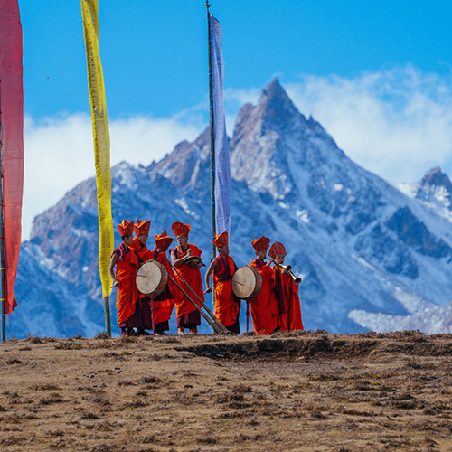Monks in orange robes with prayer flags at the Royal Highland Festival, Himalayan peaks behind
